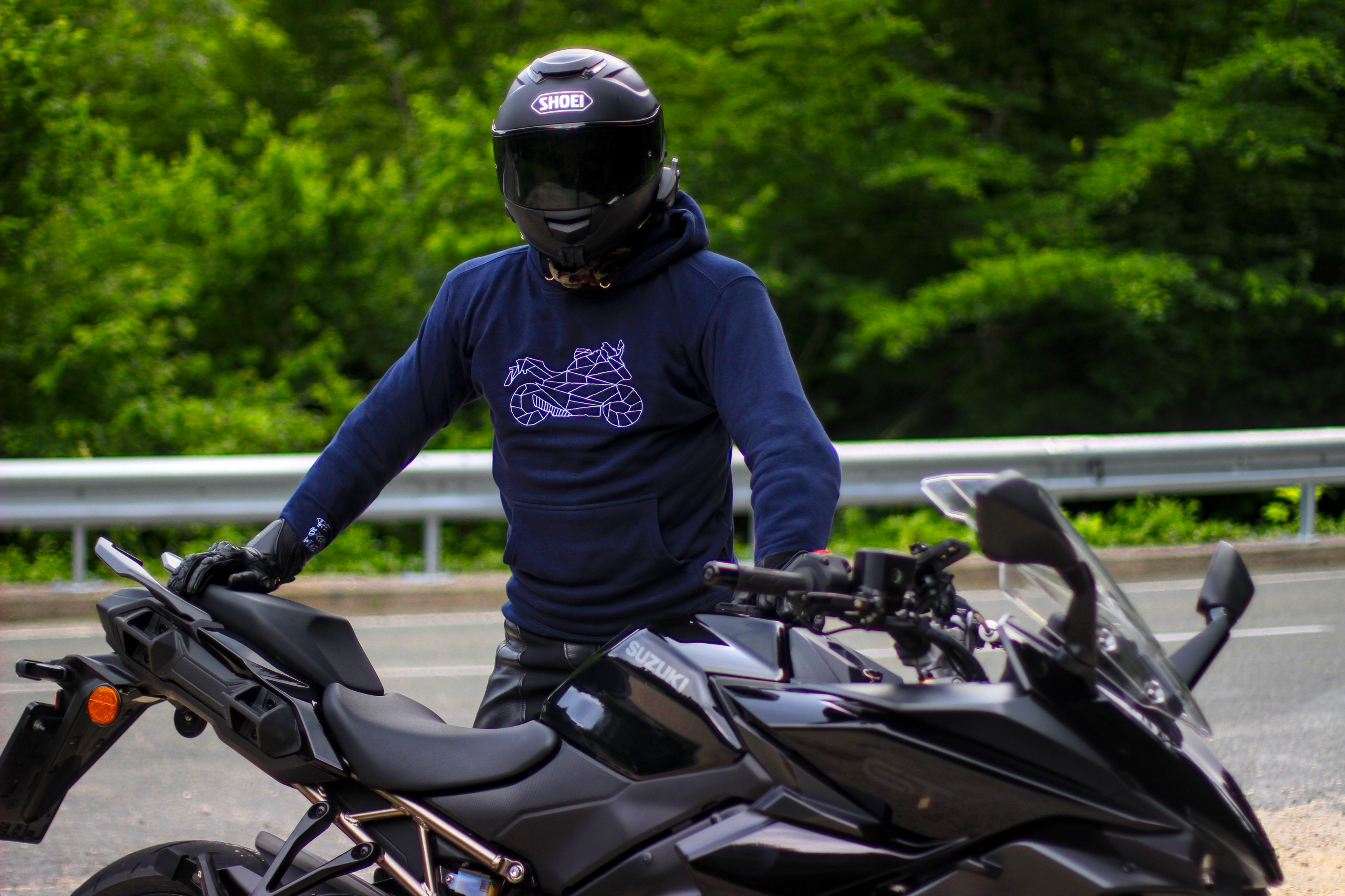 The Biker Mule motorcycle style hoodie worn by rider standing next to black sport motorcycle on road