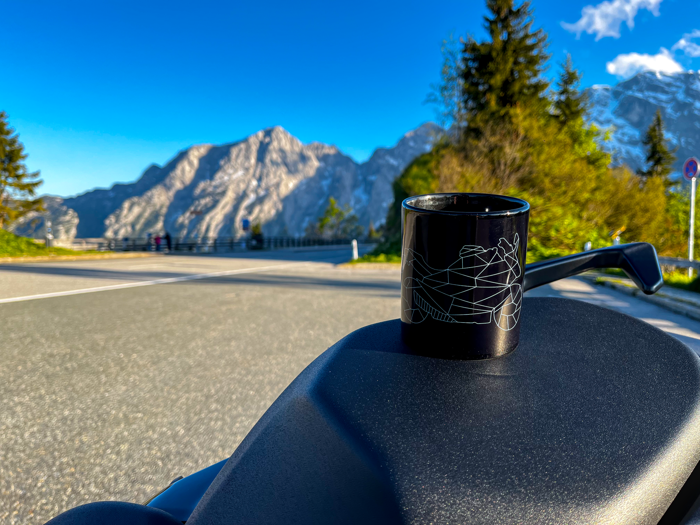 Black motorcycle style mug with geometric bike design on motorcycle seat against mountain background