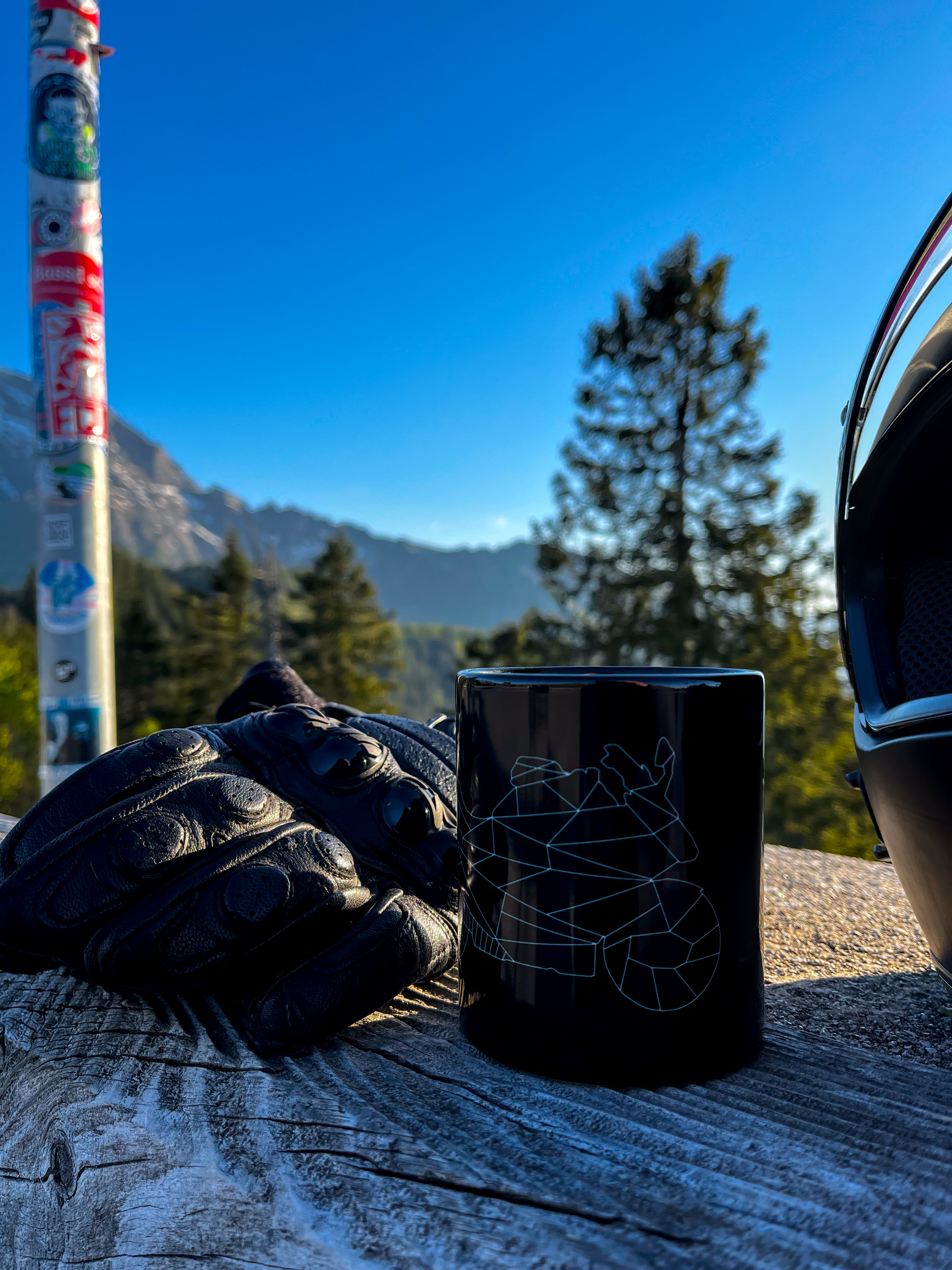 Black mug with motorcycle design next to leather gloves and helmet in outdoor setting motorcycle enthusiast gifts