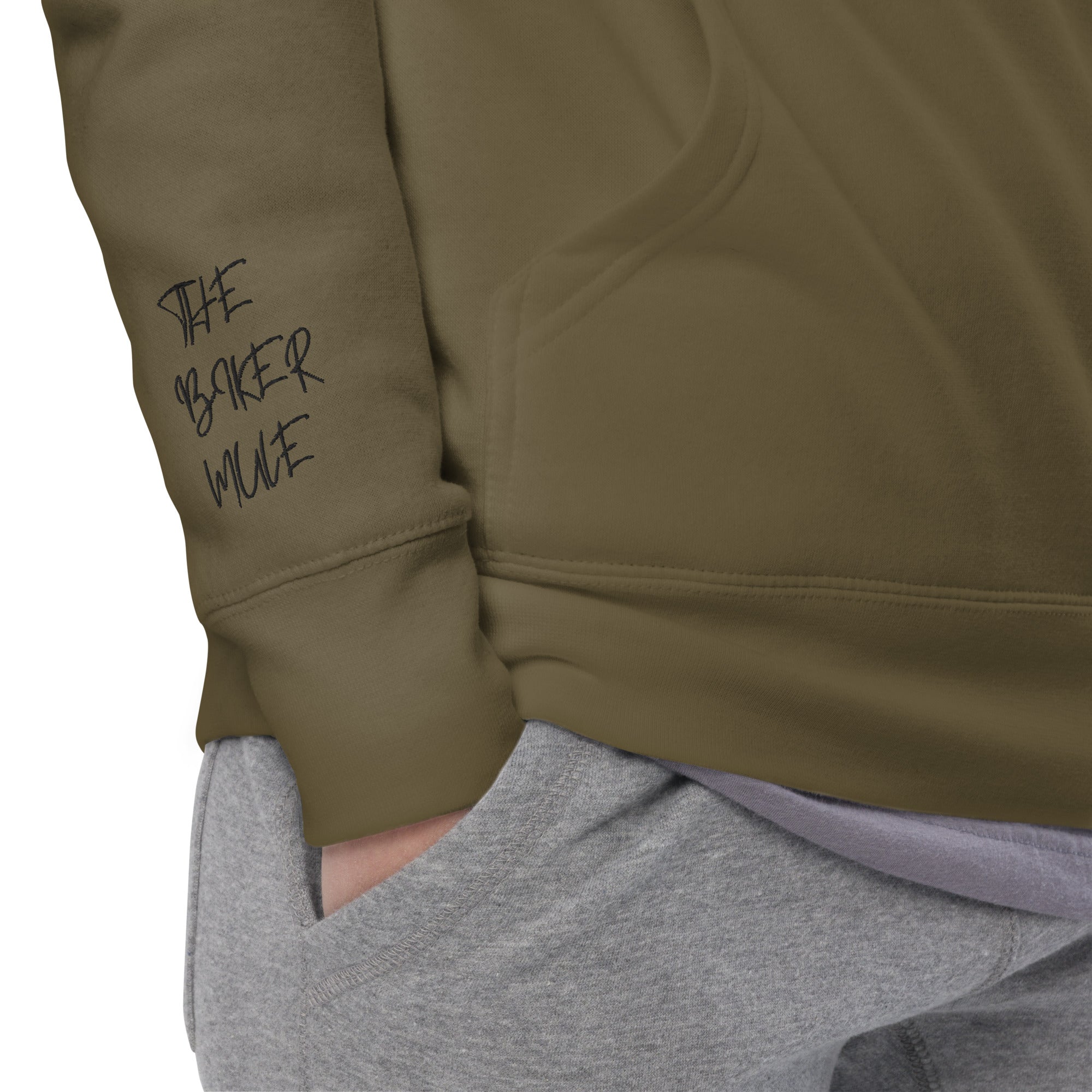 Close-up of olive green motorcycle hoodie unisex sleeve with The Biker Mule logo and hand in gray pants pocket