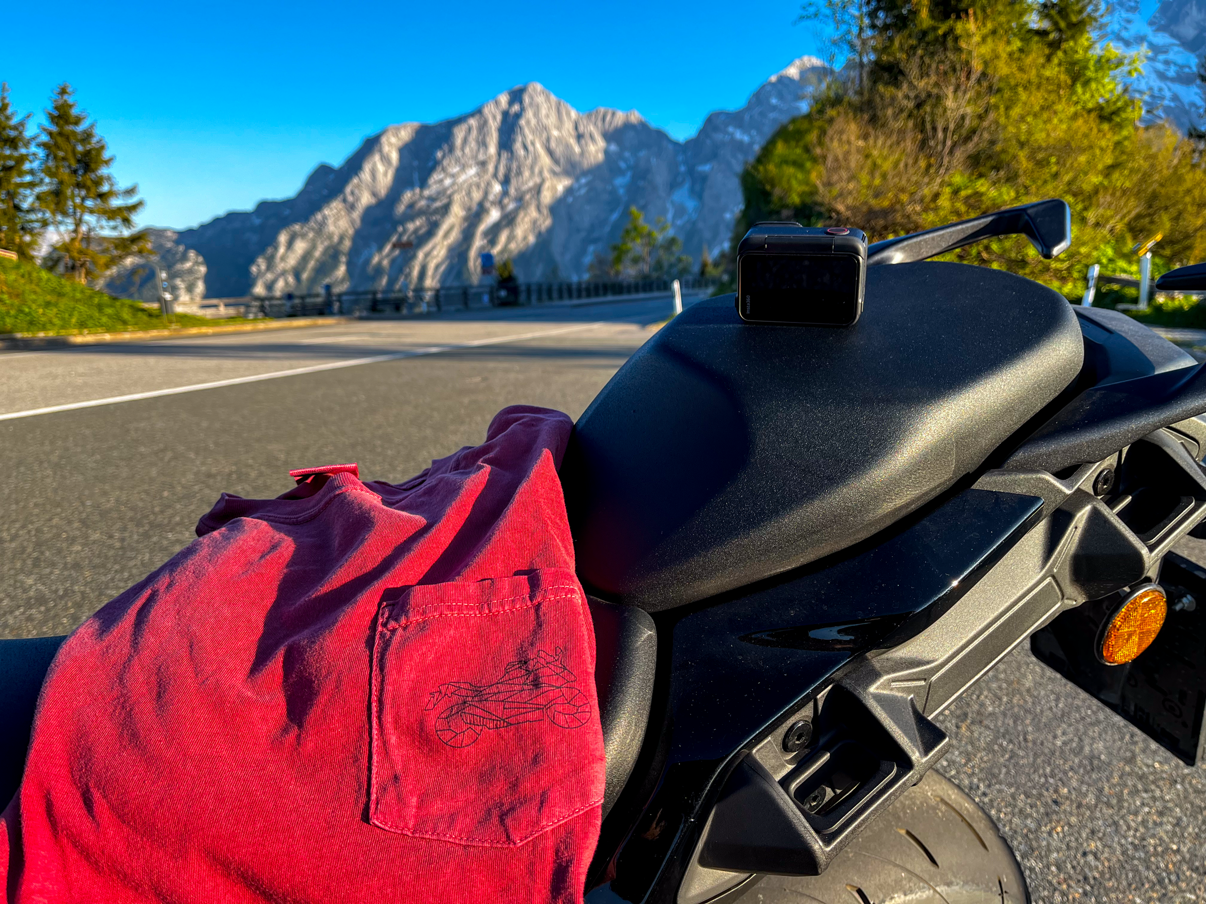 Red motorcycle pocket shirt for men draped over black motorcycle seat with mountain backdrop