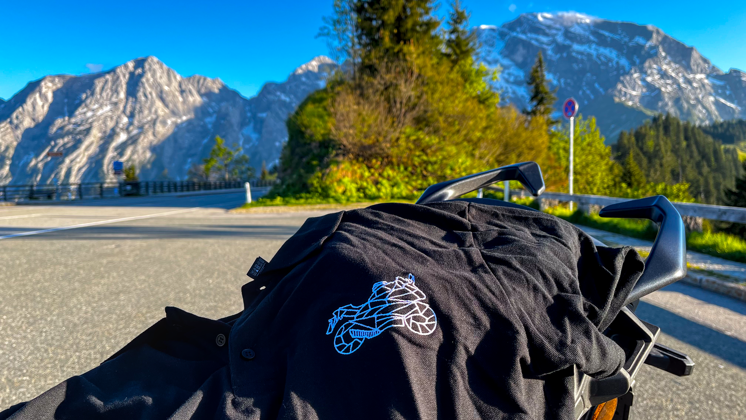 Black motorcycle polo shirt for men with white logo detail from The Biker Mule on a scenic mountain road