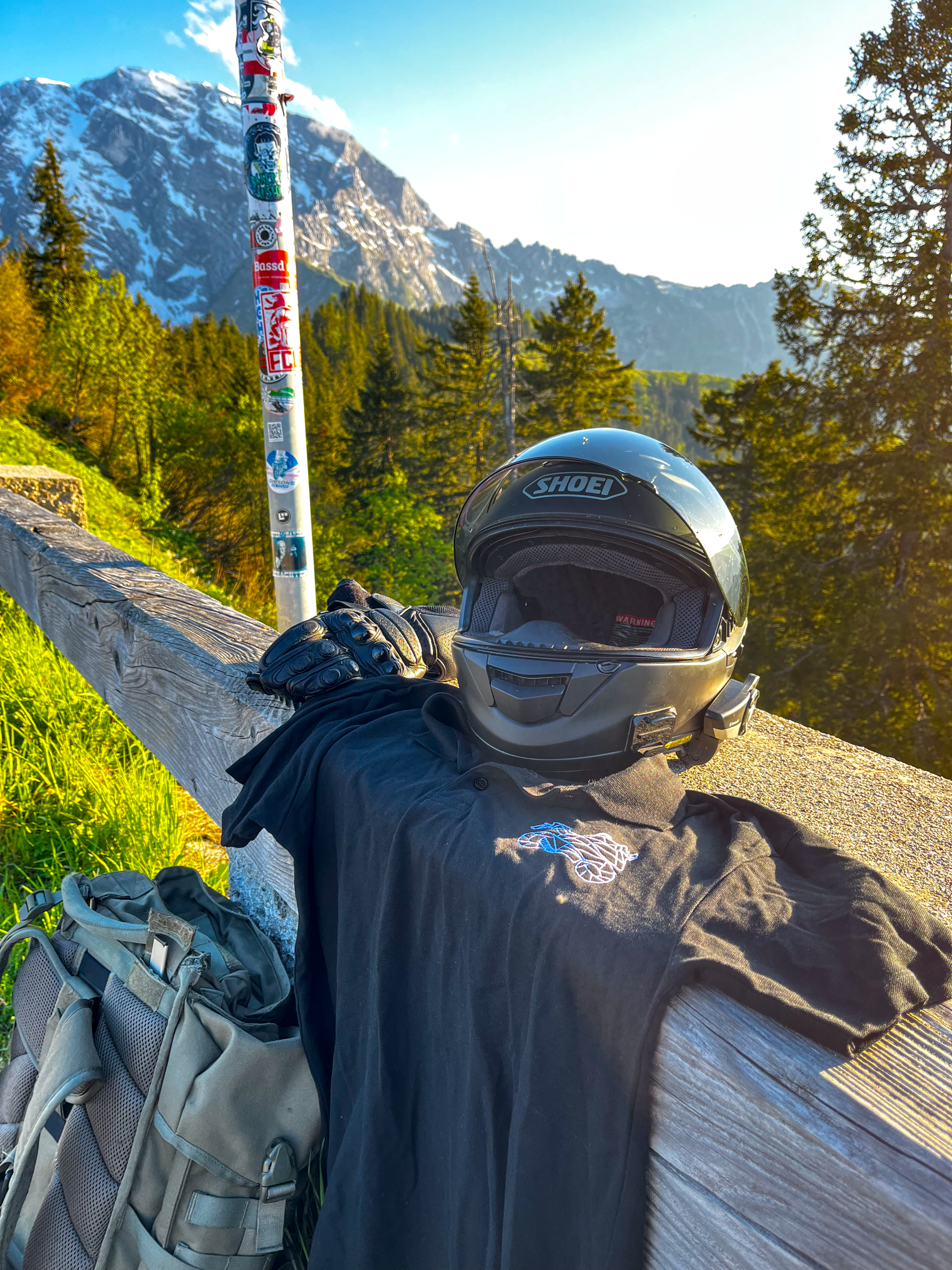 Motorcycle polo shirt men in black by The Biker Mule displayed with helmet and gloves on wooden fence in mountainous outdoor setting