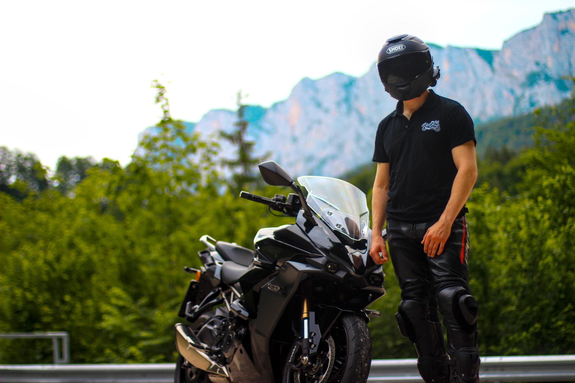 Man wearing motorcycle polo shirt men by The Biker Mule standing next to a black sport motorcycle with mountains in background