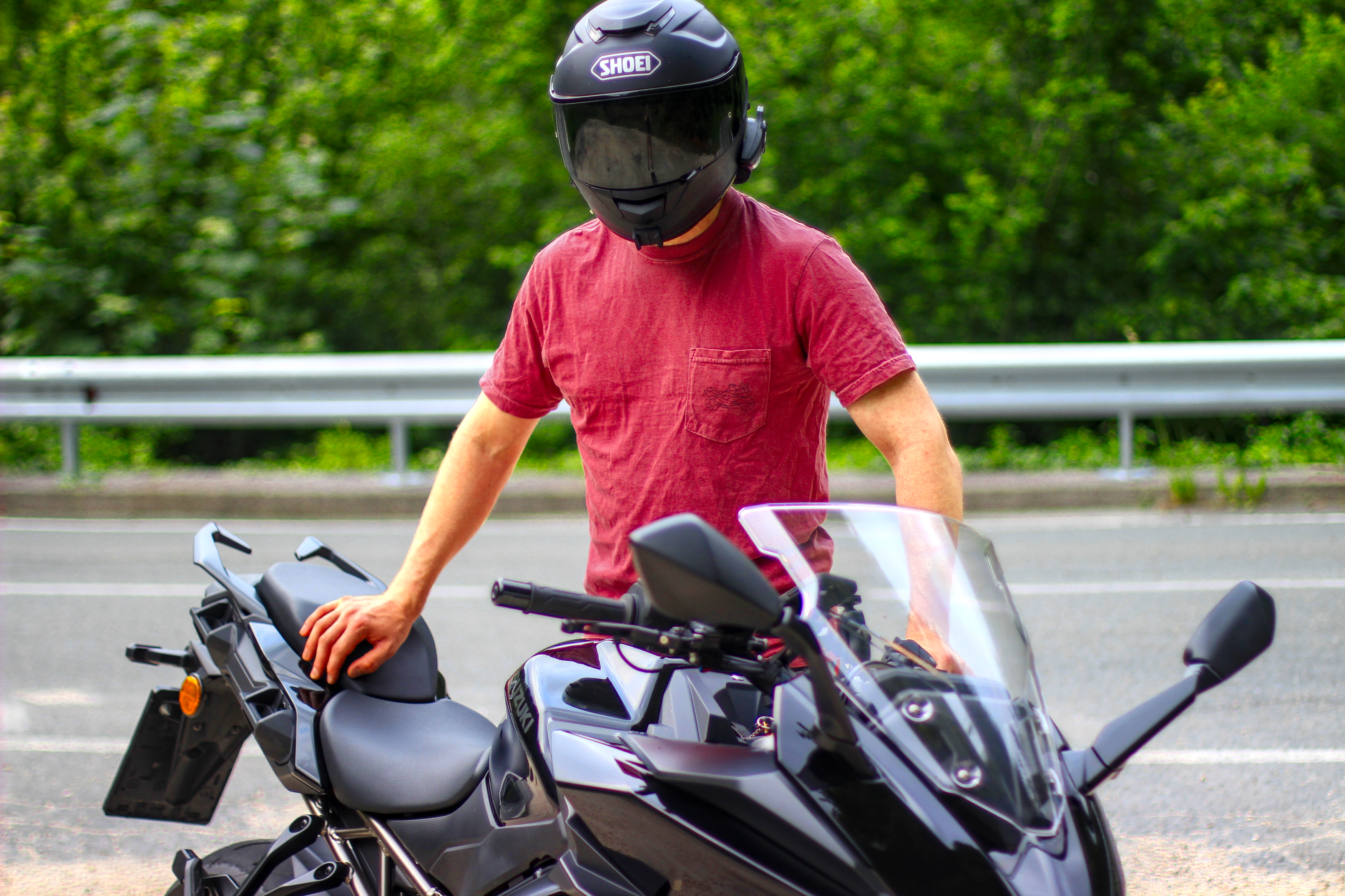 Man wearing a red motorcycle pocket shirt and black helmet standing next to a black motorcycle on the road